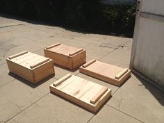 four wooden boxes sitting on top of a cement floor next to a building and bushes