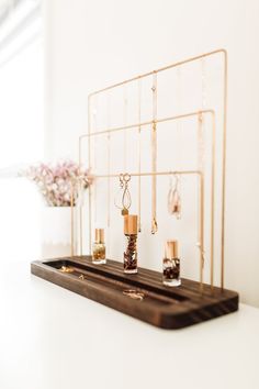 a wooden tray topped with bottles filled with jewelry next to a flower vase on top of a white table