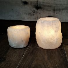 two white candles sitting on top of a wooden table next to each other and one is lit