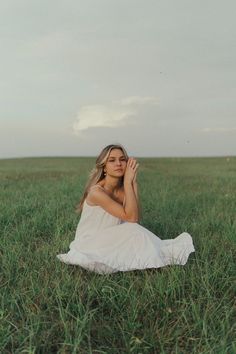 a woman sitting in the middle of a field with her hands up to her face