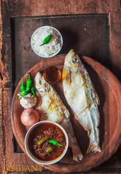 two fish are on a plate with some sauces and garlic next to it, along with other food items