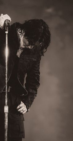 a man with long hair holding a microphone in his right hand and looking down at the ground