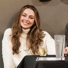 a woman sitting at a table with a glass of wine in front of her and a man standing next to her