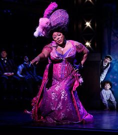 a woman in a purple dress on stage with other people behind her and one man standing next to her