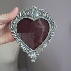 a person holding up a heart shaped mirror in front of a white wall with an ornate frame