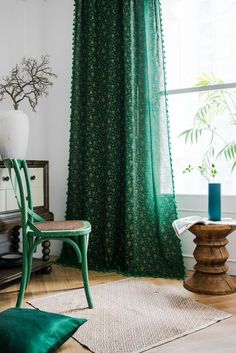 a green chair sitting in front of a window next to a wooden table with a vase on it