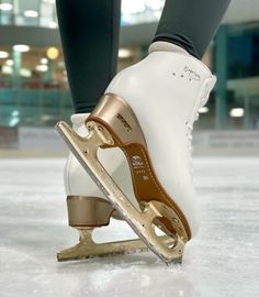 a person wearing white and gold ice skates with their feet on an ice rink