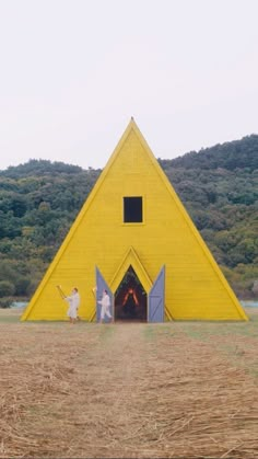 two people standing in front of a large yellow triangle shaped structure with doors and windows