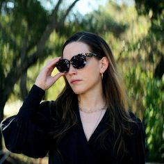 a woman with sunglasses on her head looking off into the distance while standing in front of trees