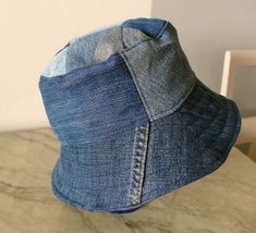 Blue jeans bucket hat. For him or her. This hat is made from upcykled blue denim. I sewn it on my lovely vintage sewingmachine. And yes, you can tell this item is handmade and quite unike.  It has a small  zipper pocket and several seams from the fabric, wich use to be trousers. The top of this hat is made from small patches. Inside has a cord in a canal in the lining Inside lining is from light lilac cotton. You can wash in machine, 40 celicius and iron the brim. The brim is sturdy enough to be a good sunscren, and soft enough to sleep comfy on the bus. This hat is a medium size, about 57-58 cm/22,8-23 inch, and it is totaly unike, like you! It is handmade by me, and labeled "carrot". The carrot label is for things I sew from upcykled fabrics, and stands for eco-friendly items.  It will b Denim Blue Bucket Hat With Short Brim, Dark Wash Denim Bucket Hat, Outdoor Denim Blue Hat, Brimmed Denim Blue Bucket Hat, Denim Blue Brimmed Bucket Hat, Denim Blue Cotton Bucket Hat With Curved Brim, Denim Bucket Hat, One Size Fits Most, Blue Denim Bucket Hat With Short Brim, Brimmed Cotton Hat In Denim Blue