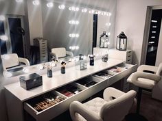 a white dressing table with lights on it and two chairs in front of the mirror