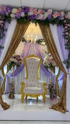 a white chair sitting in front of a purple and gold decorated stage with flowers on it