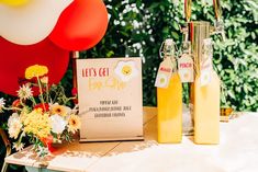 a table topped with bottles of lemonade and flowers next to a sign that says let's get egg shop