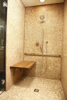 a walk in shower sitting next to a wooden bench under a light fixture on a tiled wall