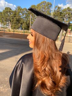 a woman with long hair wearing a black graduation cap and gown in the sun on a sunny day