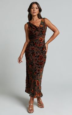 a woman in a brown floral print dress with her hands on her hips, posing for the camera