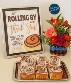 there are some cinnamon rolls on a tray next to a sign that says, just rolling by thank you