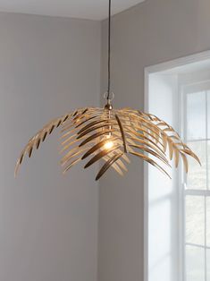 a light hanging from a ceiling in a room with white walls and palm leaves on it