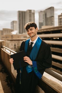 a young man in graduation gown standing on the side of a bridge with his diploma