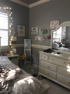 a bedroom with a bed, dresser and mirror in the corner is lit up by fairy lights