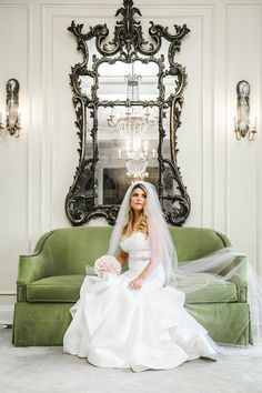 a bride sitting on a green couch in front of a mirror and chandelier