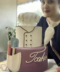 a woman standing next to a cake with the word tooke written on it and cooking utensils in front of her