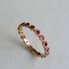 Gold Eternity ring set with Beautiful Pink Rubies. Famous for its passionate Pink-Red Color this July birthstone gemstone in one of finest and most sought after gemstones. Elegantly Set in a crown settings, Each ruby is 2mm in diameter with excellent color and clarity. This graceful Eternity ring has a dainty poise about it, getting lots of the right attention every time you wear it on its own or stack it with your other rings! Featuring between 15-22 Gemstones(Depending on ring size). Other sto Pink Ruby Stackable Jewelry, Pink Sapphire Jewelry With Halo Design, Pink Ruby Promise Ring With Halo Setting, Pink Sapphire Ring With Halo, Ruby Round Eternity Band Fine Jewelry, Anniversary Pink Sapphire Ring With Halo Design, Pink Lab-created Ruby Gemstone Jewelry, Elegant Pink Gemstone Eternity Band, Ruby Jewelry With Prong Setting For Promise