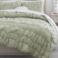 a bed with a green comforter and pillows on top of it, next to a night stand