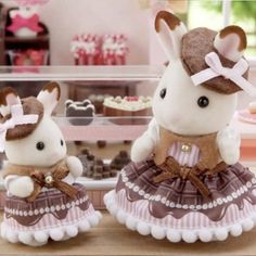 two stuffed animals dressed up in dresses on a table with cupcakes behind them