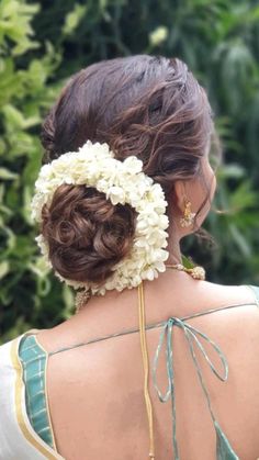 the back of a woman's head with flowers in her hair, wearing a green and white dress