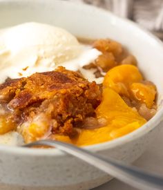 a white bowl filled with fruit and ice cream on top of a table next to a fork