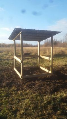 a small wooden structure sitting in the middle of a grass covered field with no people around it