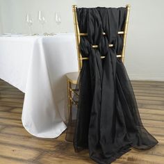 a chair with a black cloth draped over it next to a white tablecloth and wine glasses