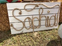 a wooden sign with rope on it sitting in the grass next to hay bales