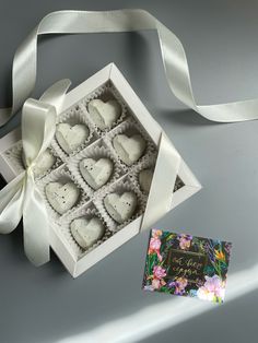 an open box of heart shaped chocolates with a white ribbon around it and a card inside