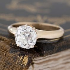 an old - fashioned diamond ring sits on top of a piece of fabric in front of a book