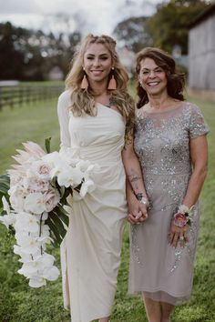 two women standing next to each other in front of a green field with white flowers