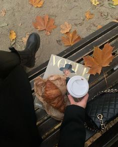 a person sitting on a bench with a coffee cup and croissant in their hand