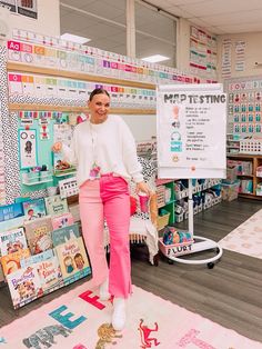 a woman in pink pants standing next to a white board with writing on it and posters behind her