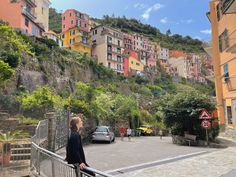 a woman standing on top of a bridge next to a lush green hillside covered in buildings