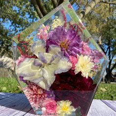 a vase filled with flowers sitting on top of a wooden table next to grass and trees