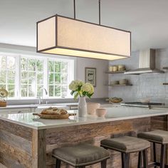 a kitchen island with stools under a hanging light over it and a bowl of bread on the counter