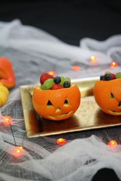 two oranges with faces carved into them sitting on a table next to some candles