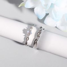 two silver rings sitting on top of a white napkin next to blue and white flowers