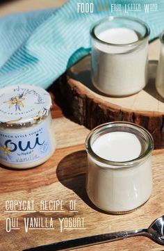 three jars of yogurt sitting on top of a cutting board next to a spoon