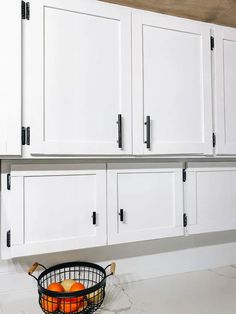 a basket with an orange in it is sitting on the counter next to white cabinets