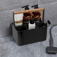 two bottles are sitting in a black container on the floor next to a tile wall