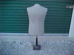 a mannequin is standing in front of a green garage door and has its head turned to the side