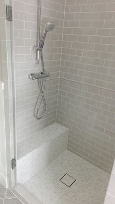 a walk in shower sitting next to a white tiled wall and floor covered with gray tiles