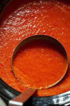 a wooden spoon is in a pot of tomato soup with red sauce on the side